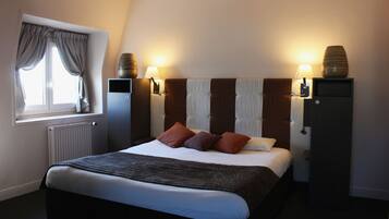 A neatly made bed with a dark headboard, two bedside lamps, and a window with curtains.