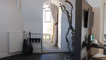 Hotelkamer met een radiator, een zwarte vaas, een plant, een televisie en een tafel met stoel op de achtergrond.