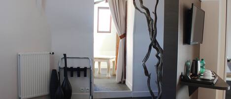 Una habitación de hotel con un radiador, un florero negro, una planta, un televisor y una mesa con una silla al fondo.