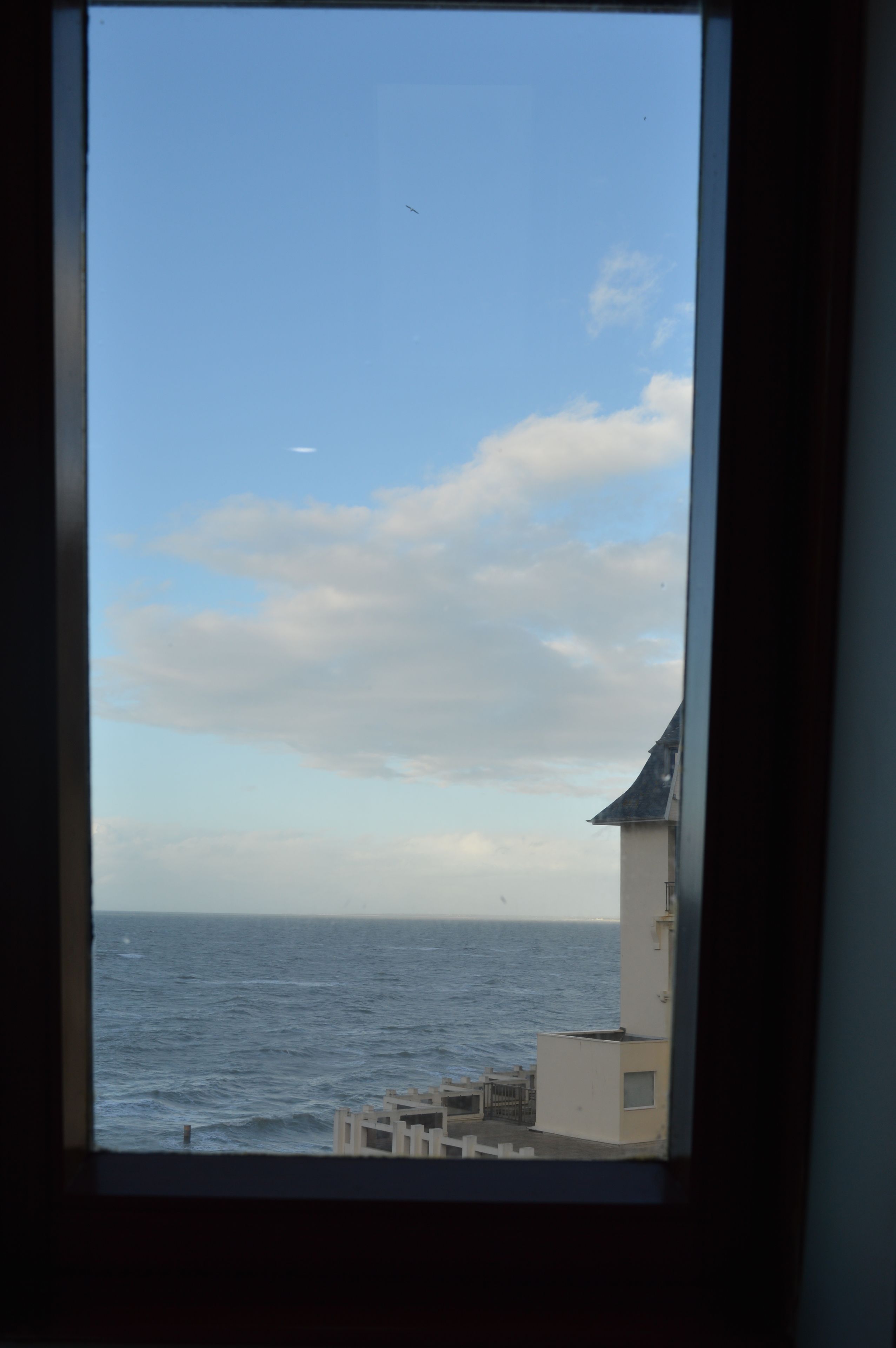 A view of the sea through a window, with a building and a clear sky.