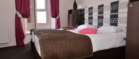 A bedroom with a bed, a nightstand, a lamp, and a dresser.