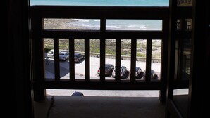 A view from a balcony overlooking a beach with the ocean and a parking area in the foreground.