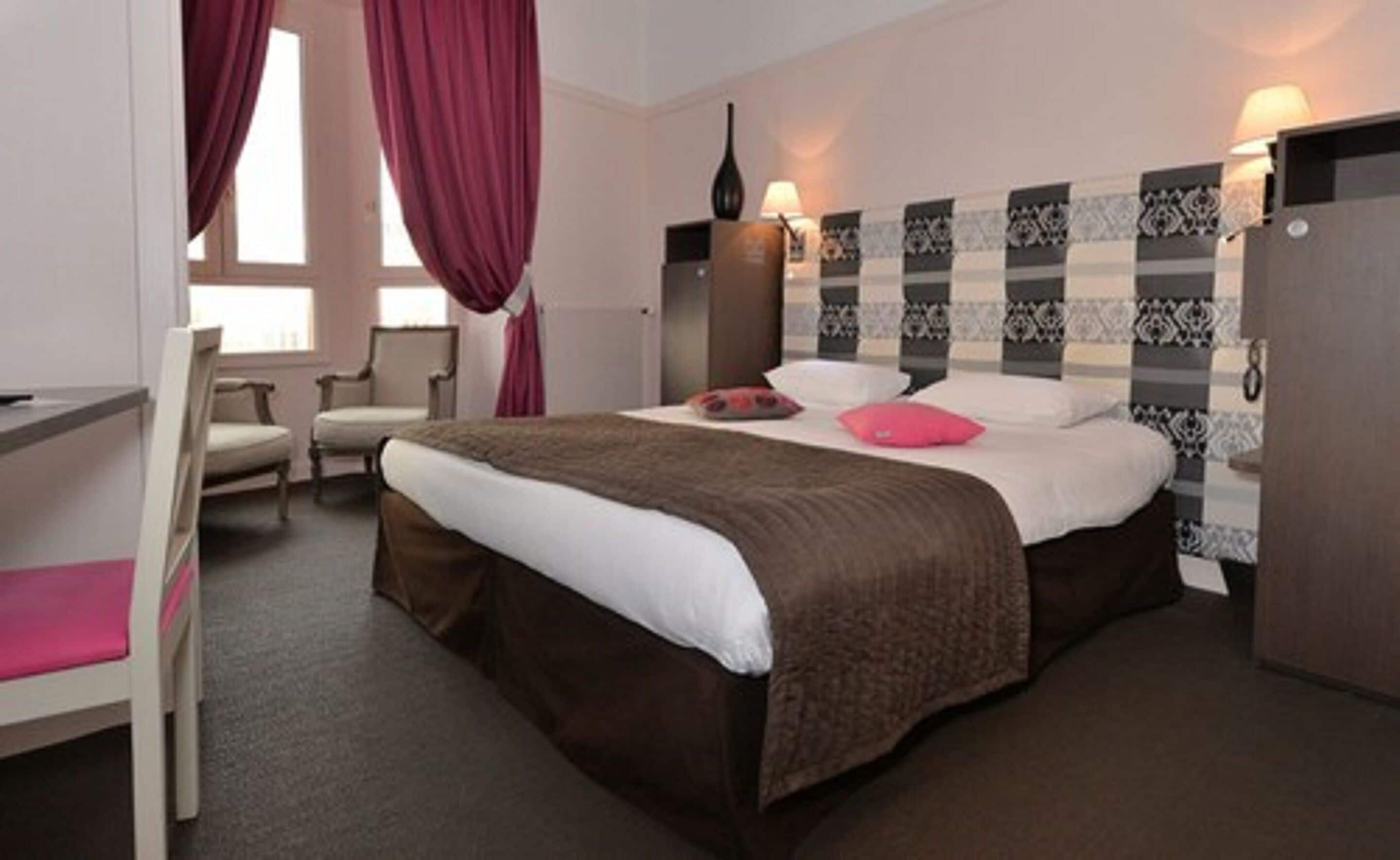 A hotel room with a bed, a chair, a desk, and a wardrobe.