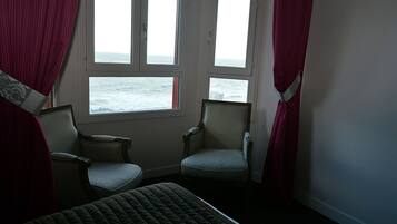 Una habitació amb un llit, dues cadires i una finestra amb vista al mar.