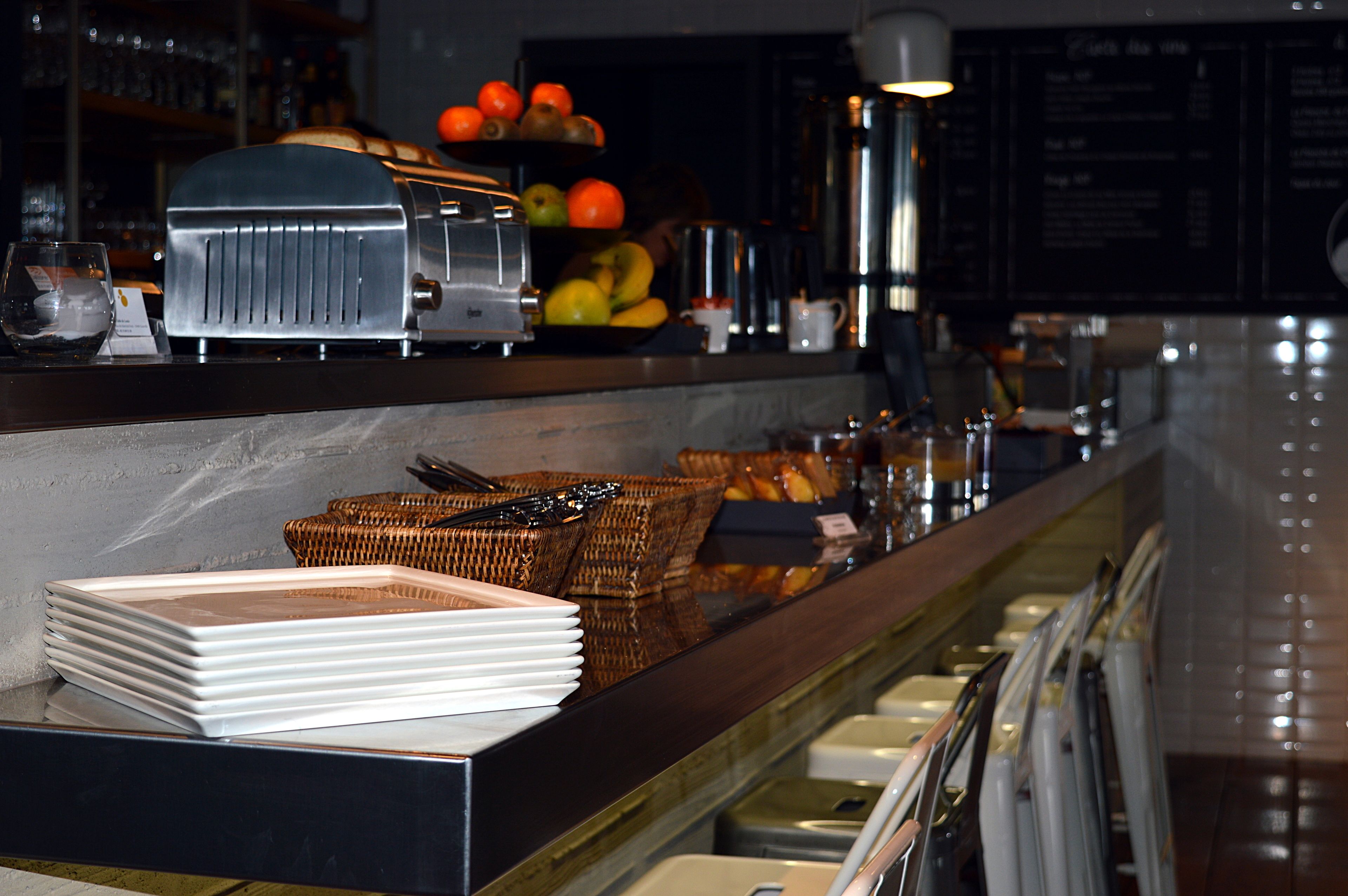 Un espace buffet proposant une variété de fruits, un grille-pain et des assiettes blanches empilées.