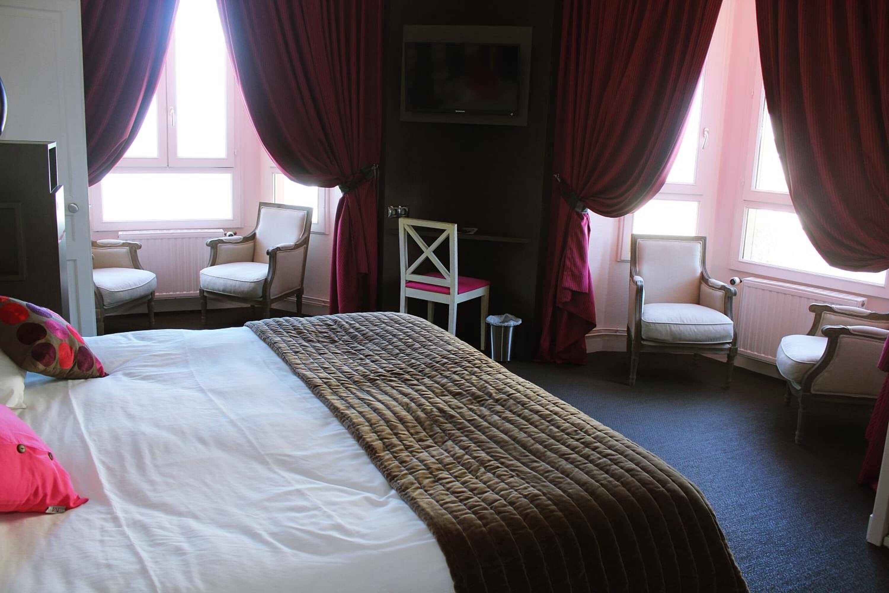 A hotel room with a bed, two chairs, a small table, and a TV on the wall.