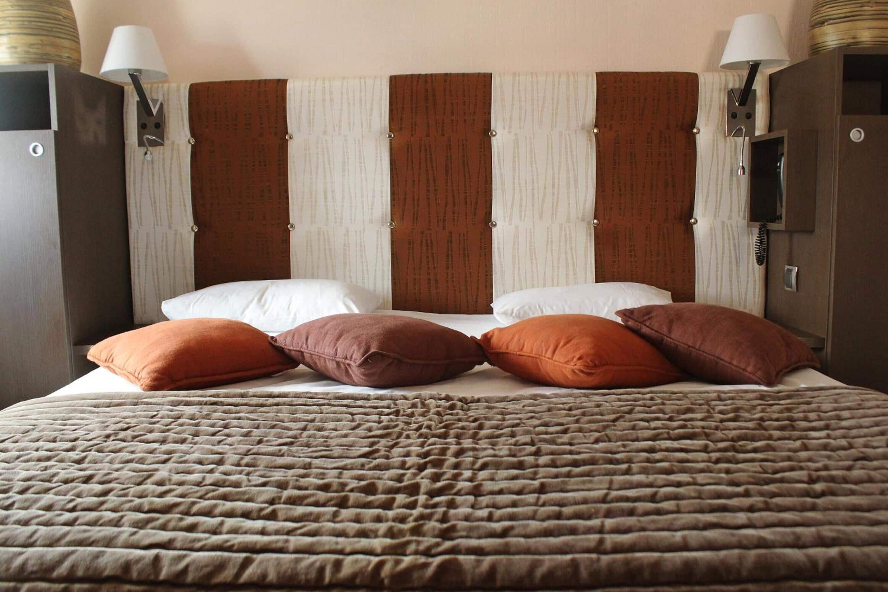 A hotel room with a large bed, multiple pillows, a headboard with vertical stripes, and wall-mounted lamps.