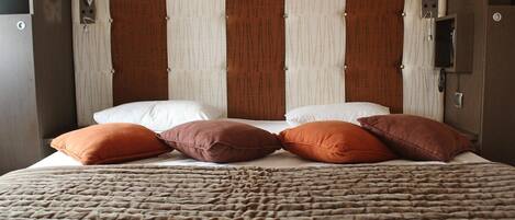 A hotel room with a large bed, multiple pillows, a headboard with vertical stripes, and wall-mounted lamps.