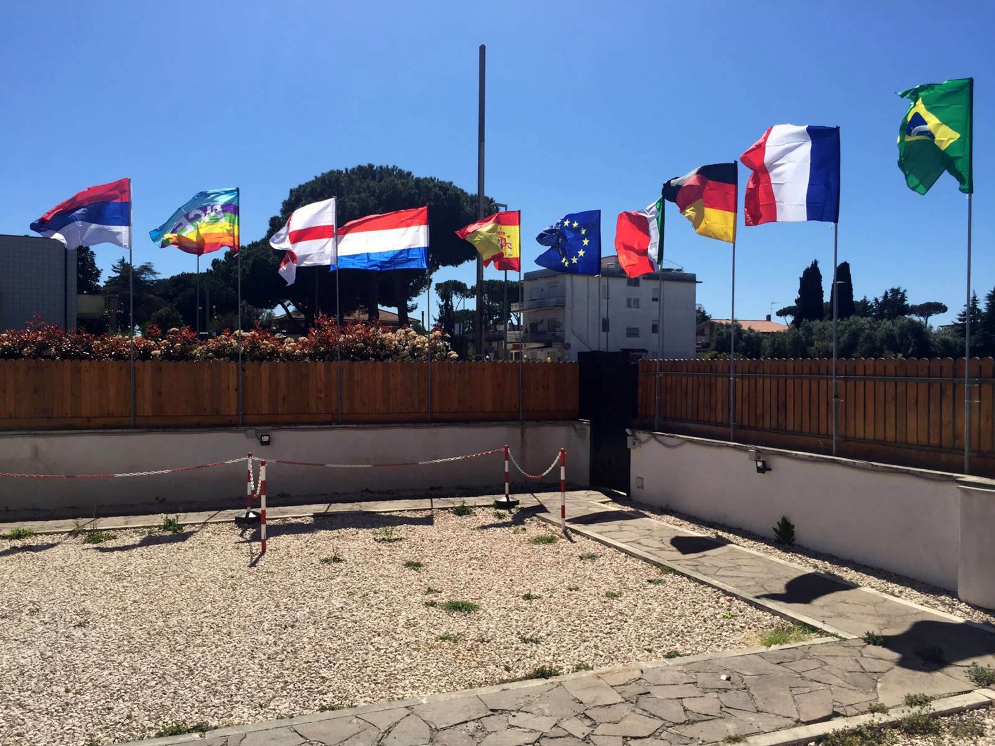 Ein Innenhof mit mehreren Nationalflaggen, einem Holzzaun und einem befestigten Bereich mit Kies.