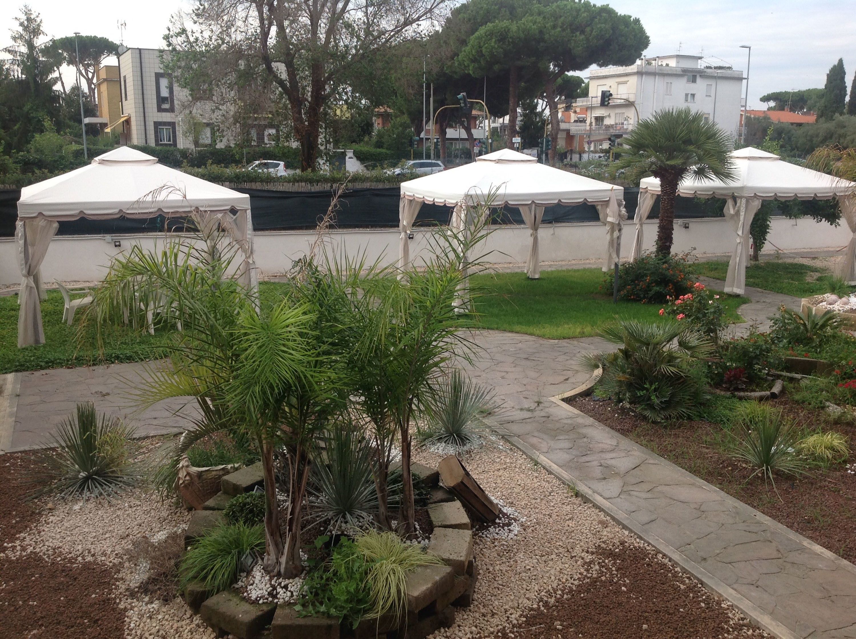 Un’area giardino con tende bianche, un vialetto lastricato e diverse piante.