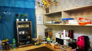 A hotel reception area with a blue curtain, a shelf with various items, a coffee machine, and a sign with text. - Il Giardino di Adriana (Terracina)