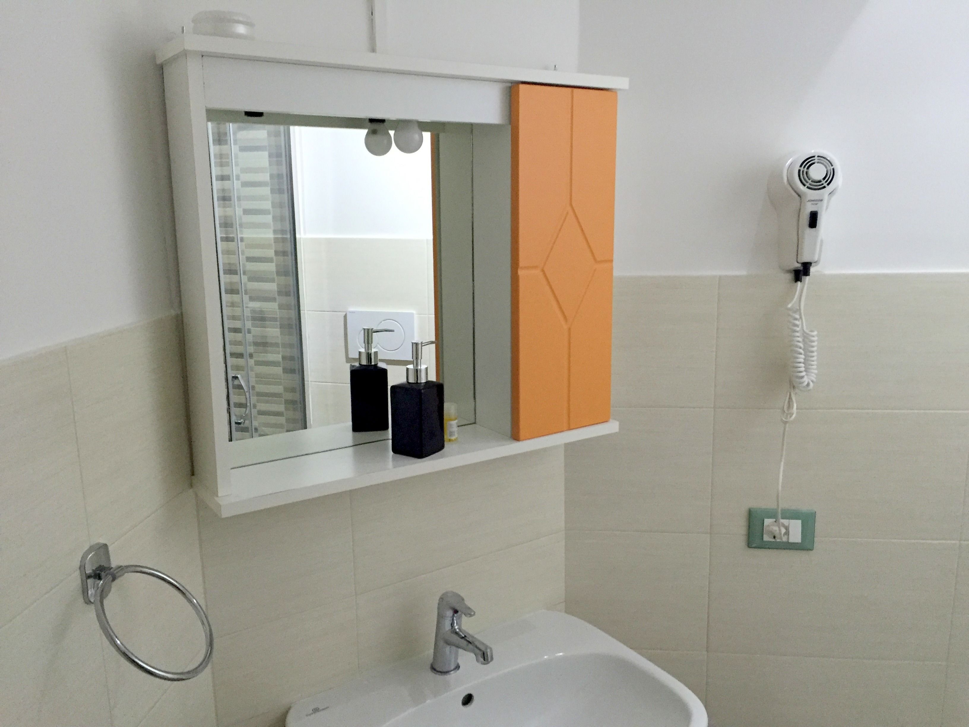 Un baño con lavamanos, espejo, secador de pelo y argolla para toallas.