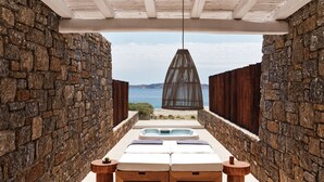 A sunlit outdoor seating area with stone walls, a wooden bench, and a table with a bowl and cup. - The Coast Bill&Coo - Adults Only (Mykonos)
