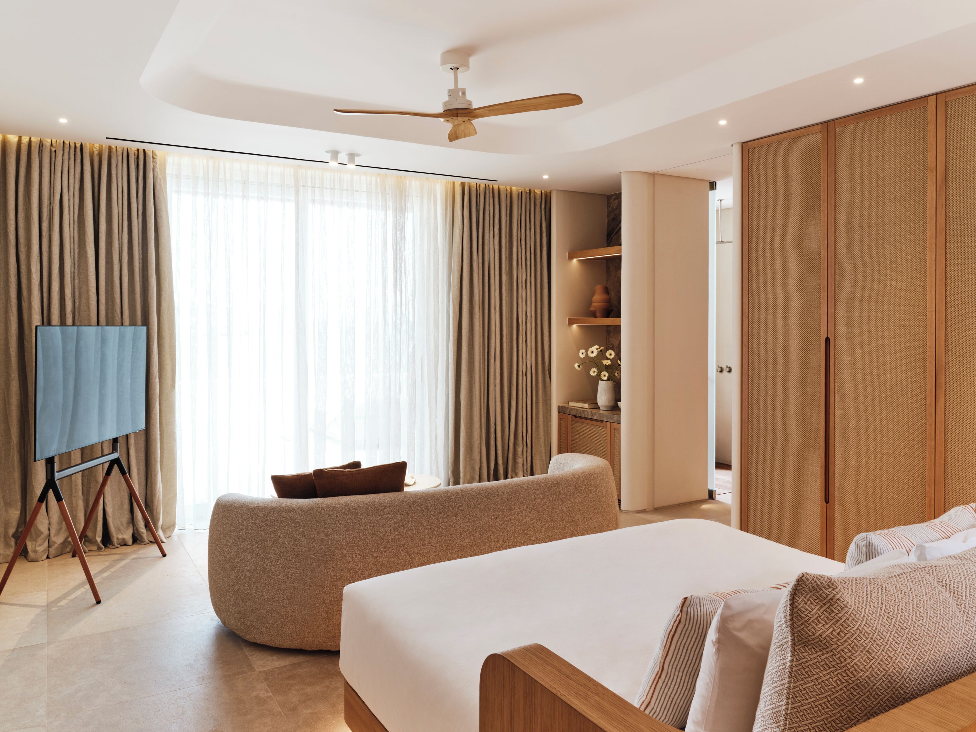 A modern hotel room with a large bed, a seating area, a ceiling fan, and a wardrobe.