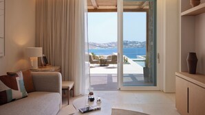 A modern living room with a sofa, coffee table, and a view of the sea through a sliding glass door. - The Coast Bill&Coo - Adults Only (Mykonos)
