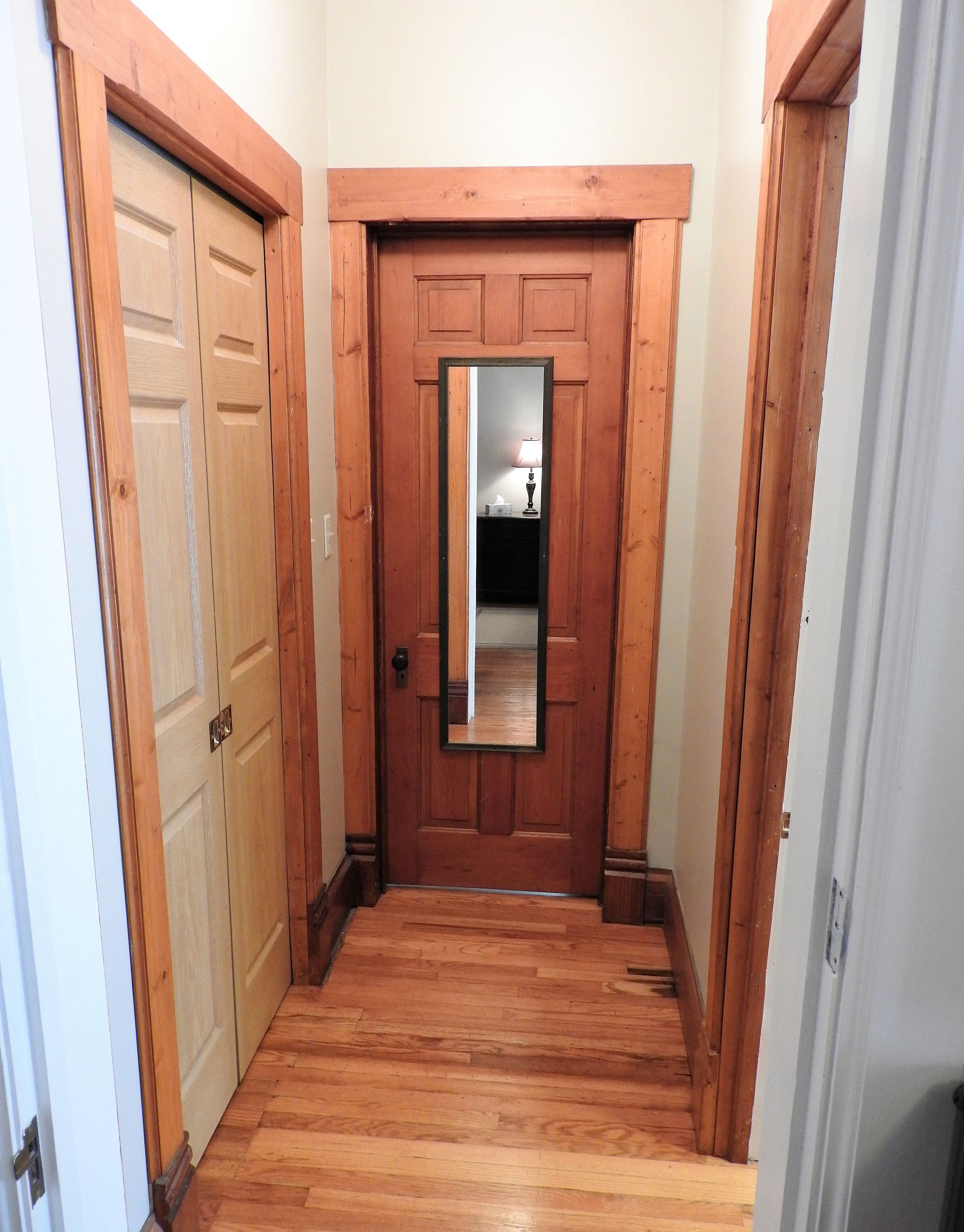 A hallway with wooden flooring and a wooden door with a mirror.