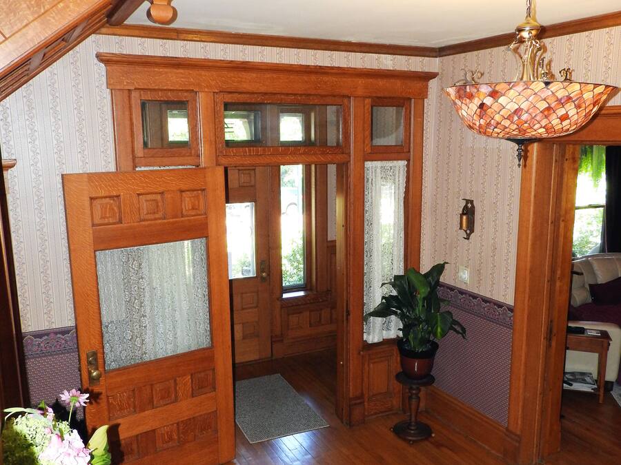 A spacious living room with wooden floors, a staircase, a chandelier, and a door leading to another room.