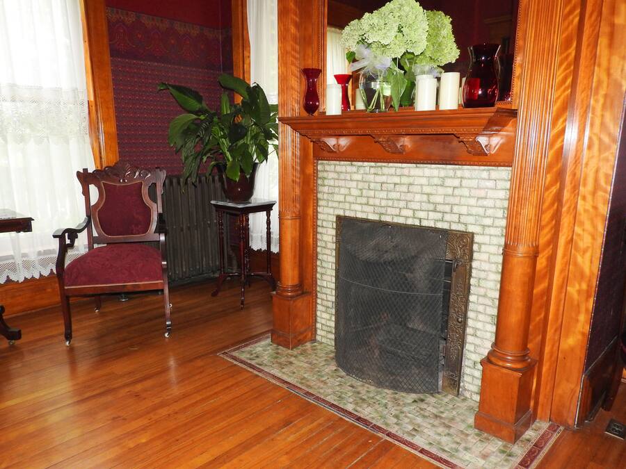 A traditional room with a fireplace, a red chair, a table, and a potted plant.