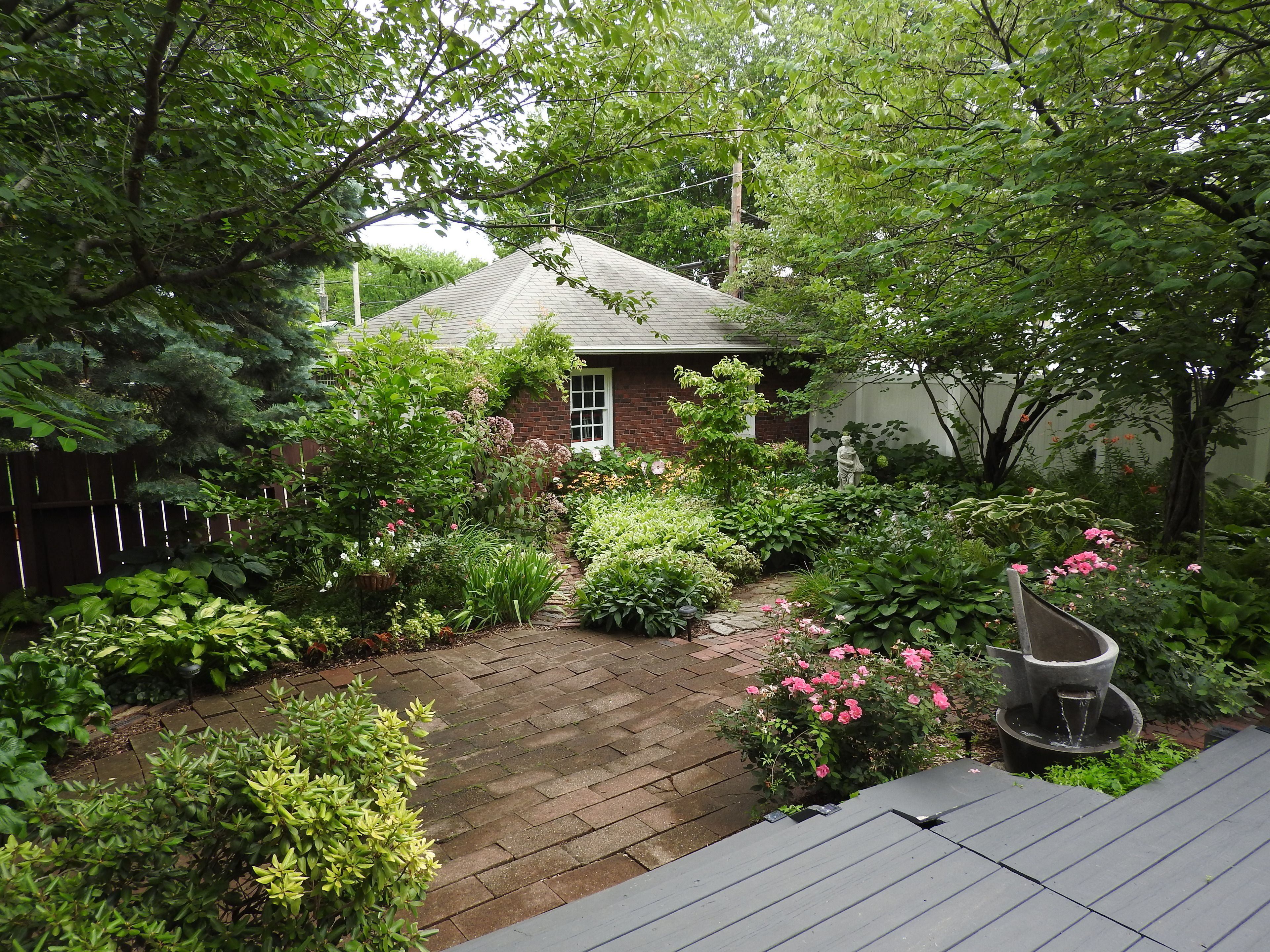 A garden with a brick pathway leading to a house with a sloped roof.