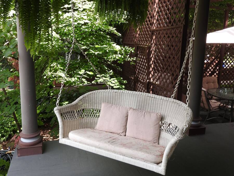 A wicker swing chair with cushions, a lattice fence, and greenery in the background.