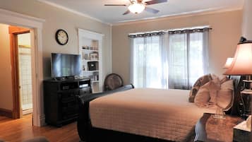 A bedroom with a bed, a ceiling fan, a TV, a bookshelf, and a window with curtains.