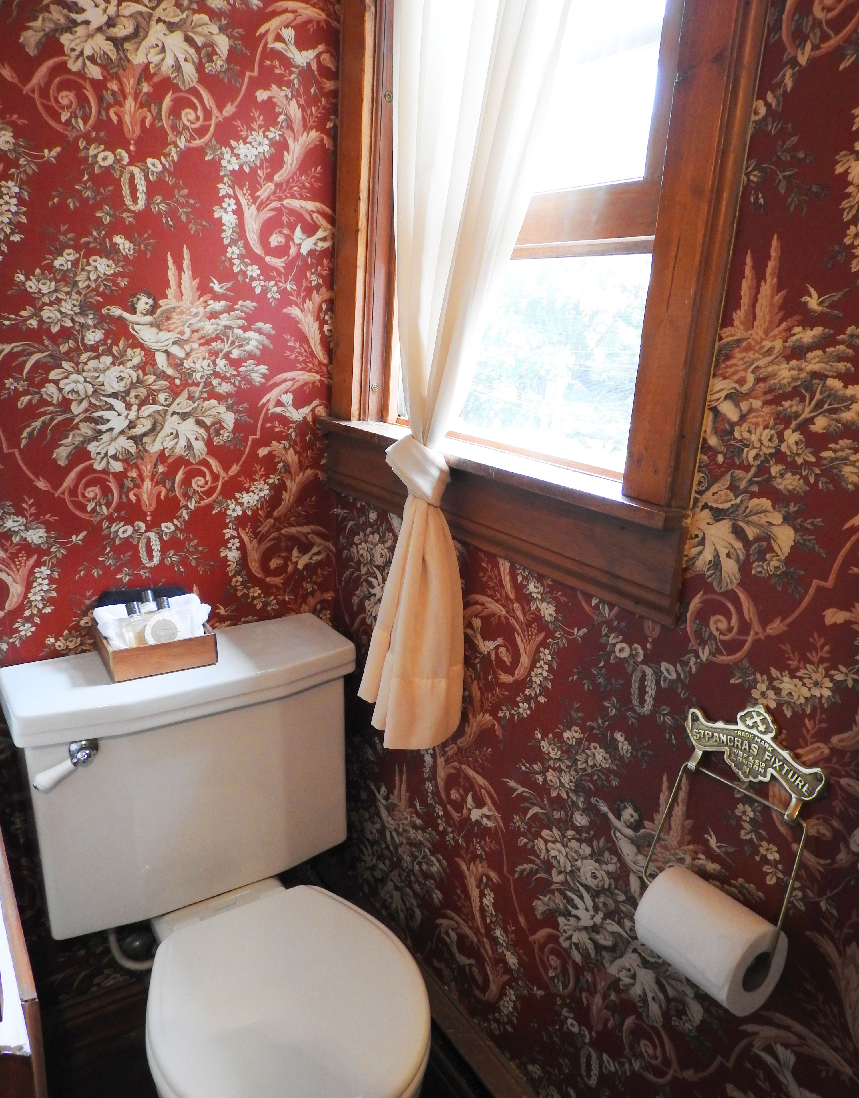 Een badkamer met toilet, toiletrolhouder en raam met gordijn.
