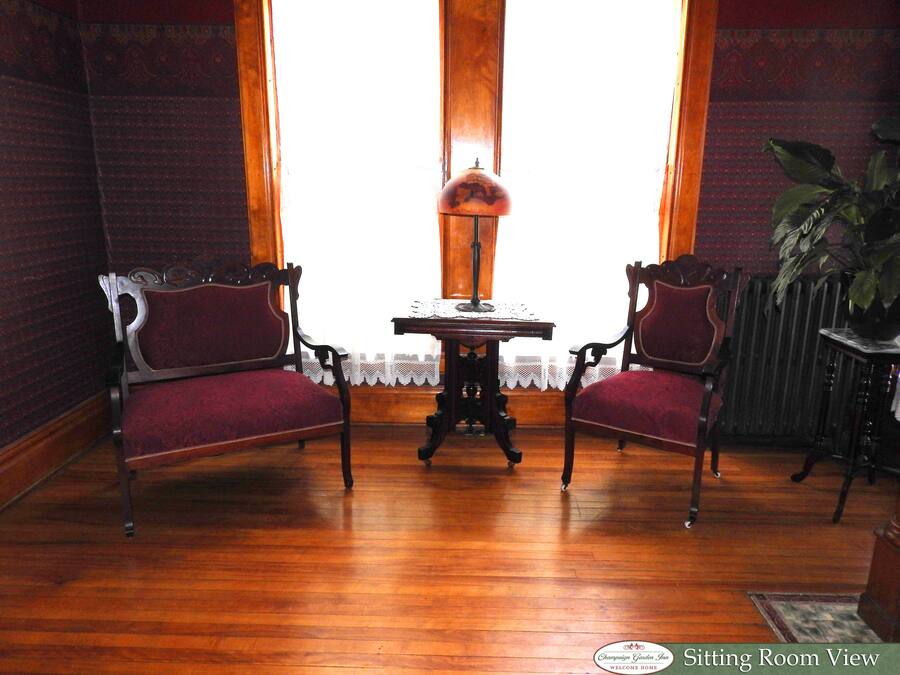 A sitting room with two chairs, a table with a lamp, and a view through a window.