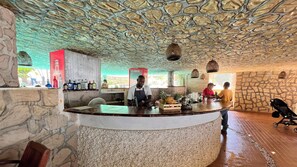 A bar area with a stone ceiling, a counter with a fan, and a Coca-Cola refrigerator. - Hotel Mendihuaca by On Vacation (Santa Marta)