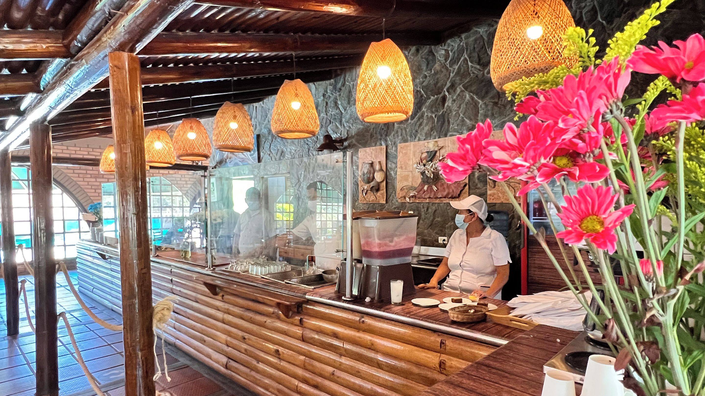 Un interior de restaurante con una barra de madera, lámparas colgantes y un jarrón grande con flores.