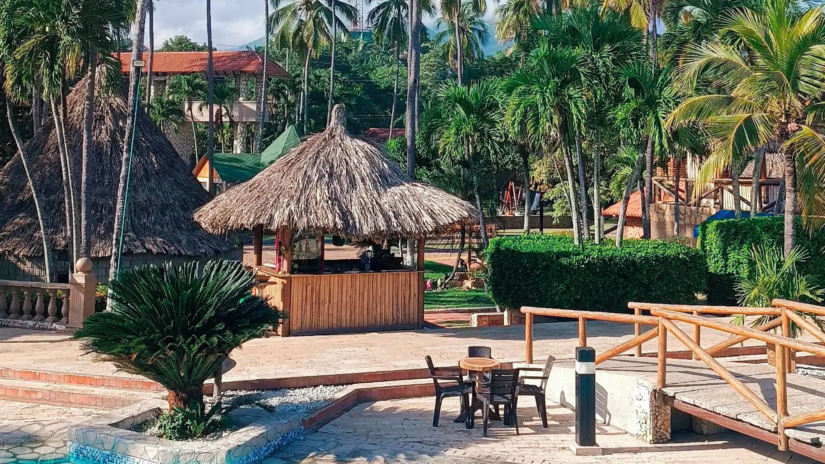 Ein tropisches Resort mit einer Struktur mit Reetdach, Sitzgelegenheiten im Freien und einem Poolbereich.