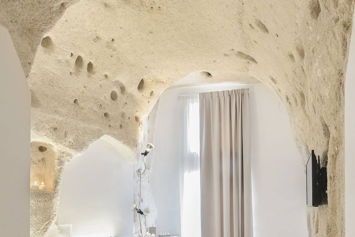 A bedroom with a unique arched ceiling, a bed, a bedside table, and a window with curtains.