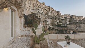 A terrace with stone flooring, white chairs, a cactus plant, and a table with a small potted plant. - La Dimora di Metello (Matera)