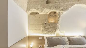 A cozy bedroom with a unique cave-like ceiling, a wooden bedside table with a lamp, and a neatly made bed.