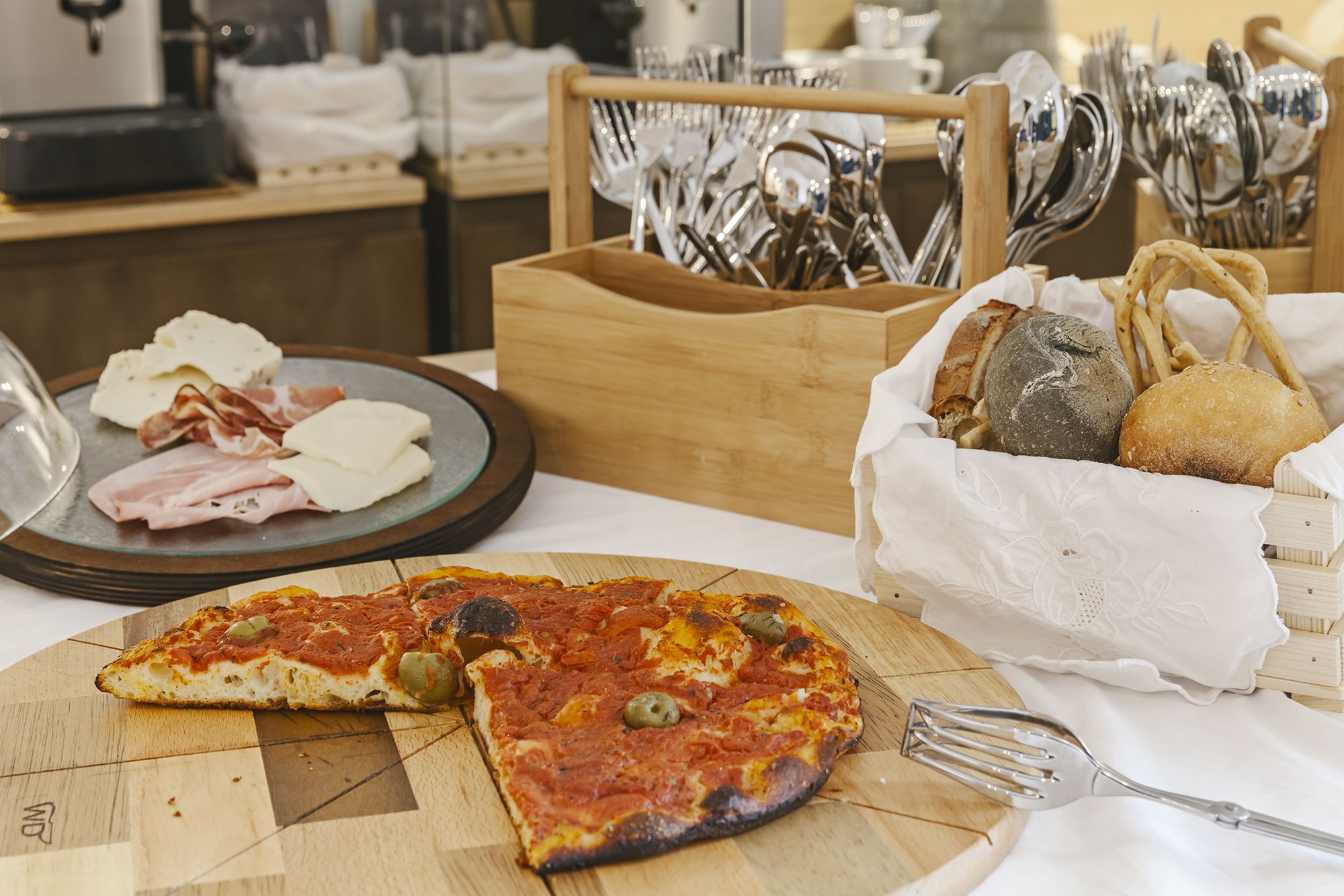 A table with a pizza, a plate of cured meats, and a basket of bread and cheese.