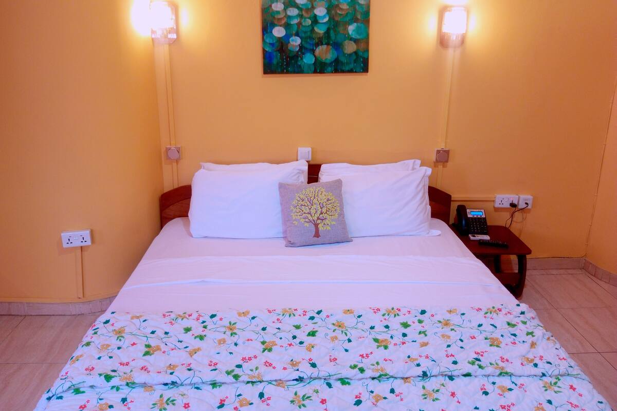 A hotel room with a bed, a nightstand, and two wall-mounted lamps.