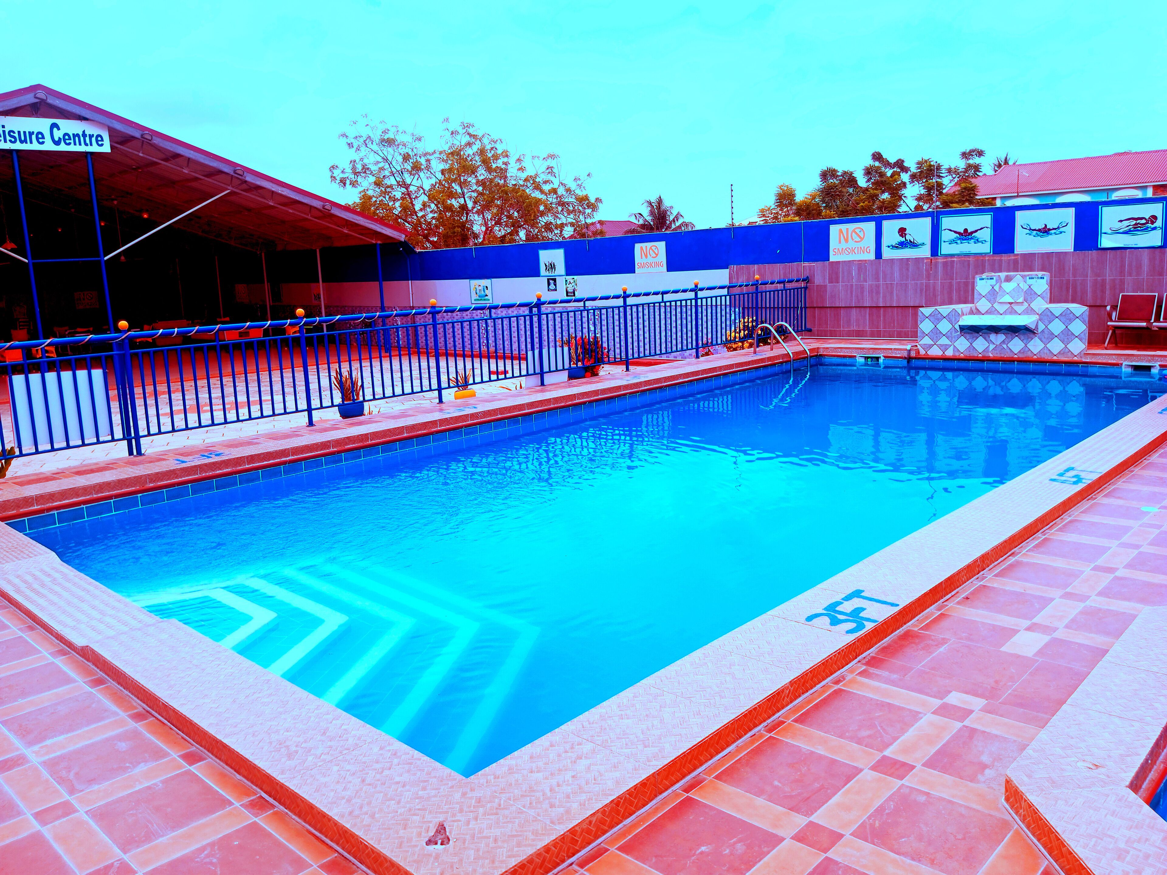 A swimming pool with a tiled deck, a covered seating area, and a sign indicating a no-smoking policy.