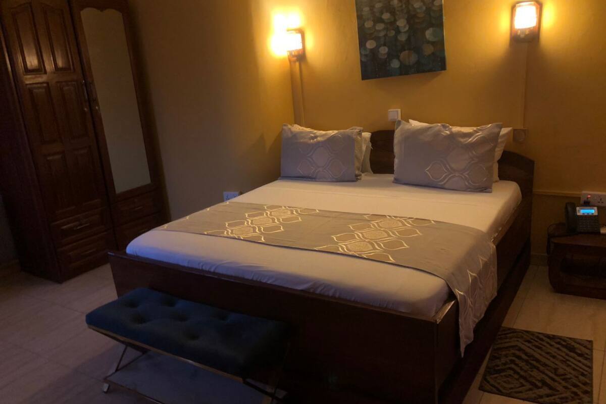 A bedroom with a bed, bedside tables, a bench, and wall-mounted lights.