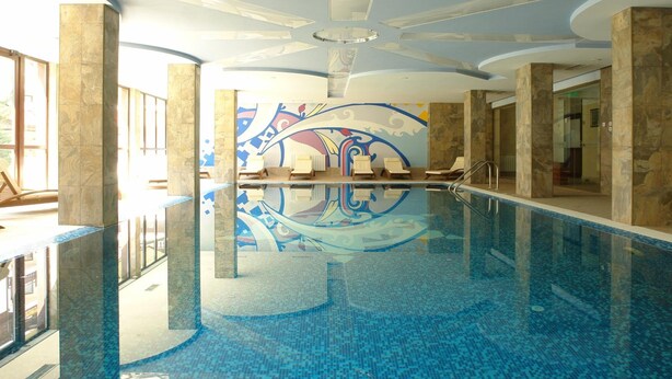 A large indoor swimming pool with clear blue water, surrounded by marble columns and a decorative ceiling.