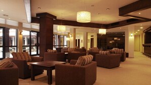 A spacious lobby with multiple sofas and armchairs, large windows, and hanging lamps.