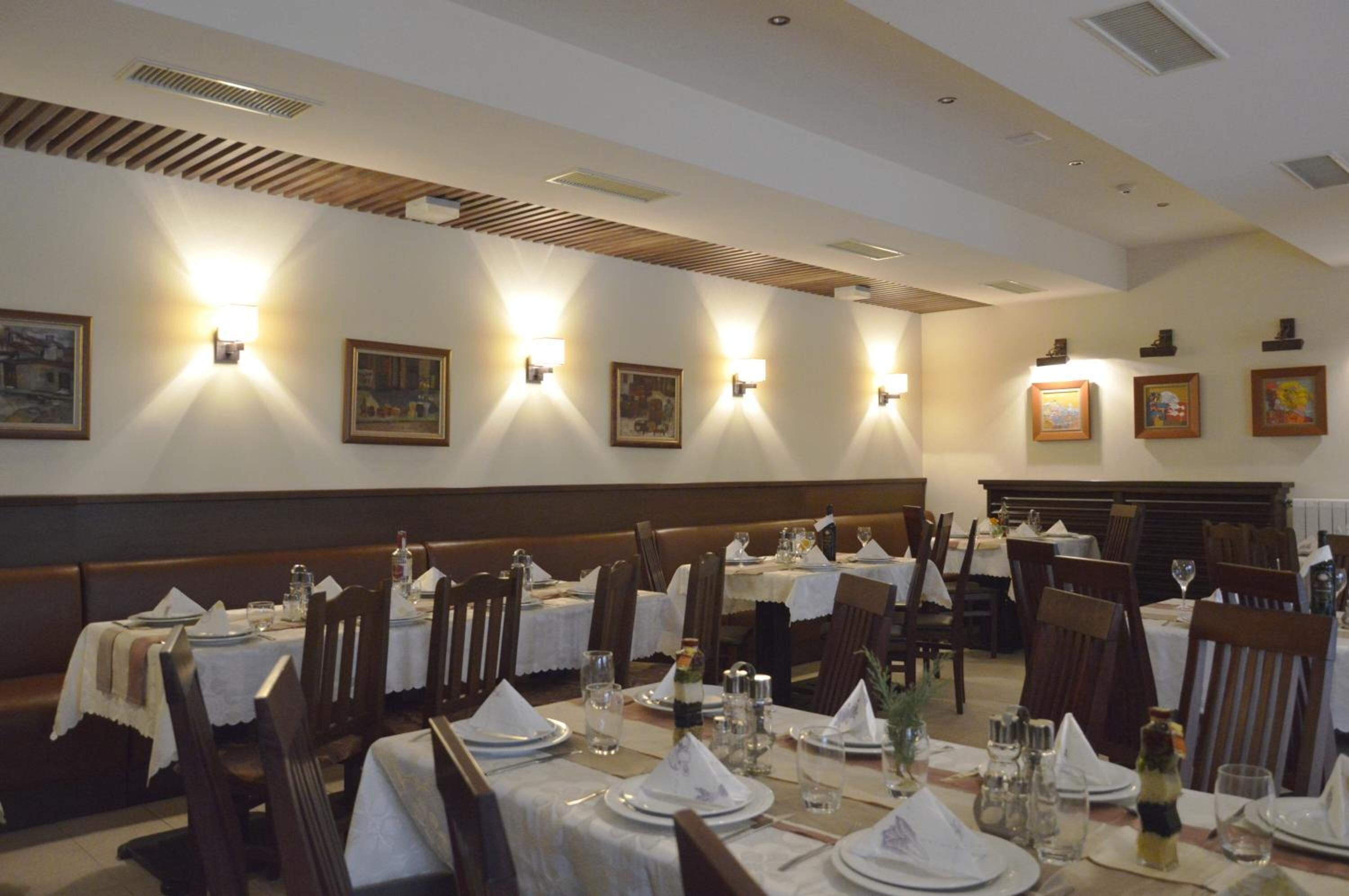 Un restaurant où de nombreuses tables sont dressées pour le service, chacune étant recouverte d’une nappe blanche et agrémentée d’assiettes, de verres et de couverts disposés avec soin.
