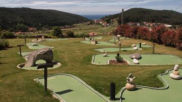 Un campo de minigolf con senderos verdes, búnkeres y un paisaje con colinas y un pueblo.