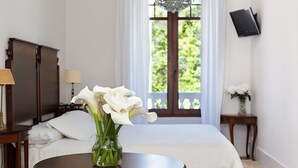 A bedroom with a bed, a vase with flowers, a television on the wall, and a window with a view of greenery. - Hotel Rústico A Torre de Laxe (Laxe)
