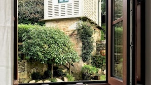 A room with a window overlooking a stone building with shutters. A vase with flowers is on a table by the window. - Hotel Rústico A Torre de Laxe (Laxe)