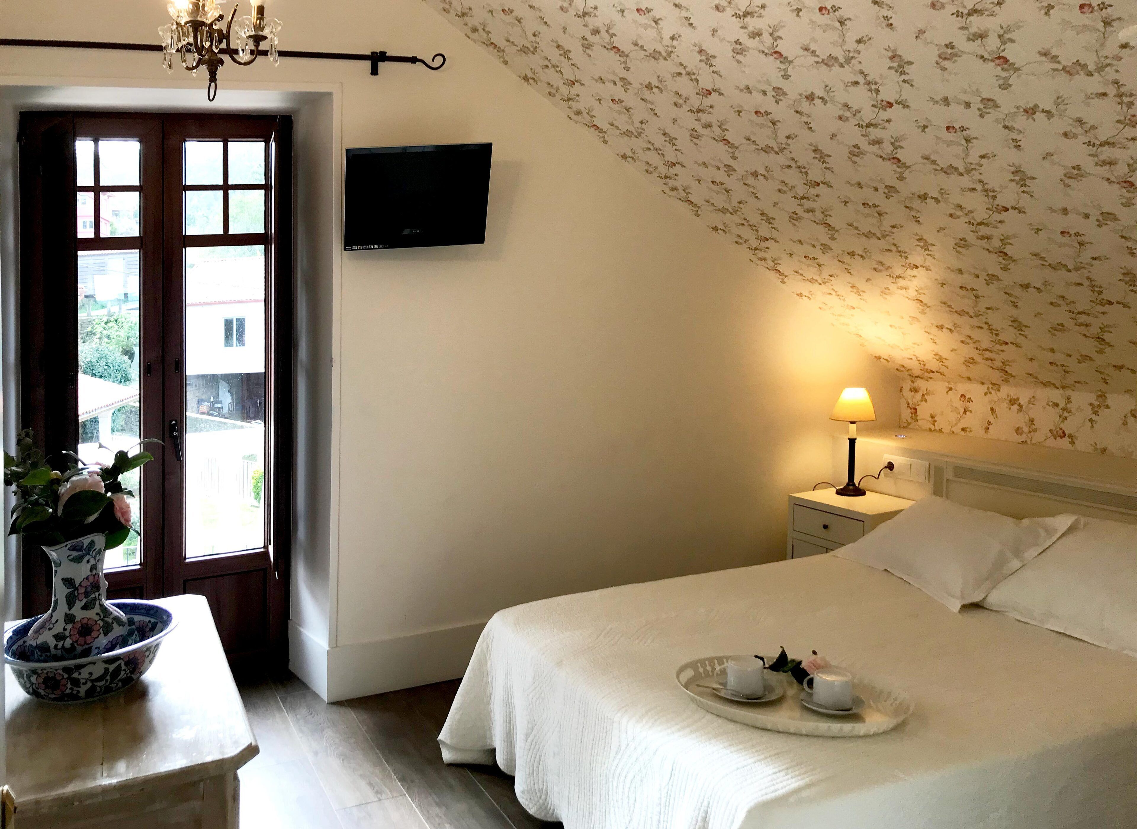 Quarto com cama, mesa de cabeceira, luminária e papel de parede estampado com flores.