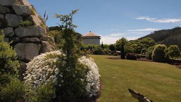 A garden with a stone wall, white flowers, and a building with a tiled roof.