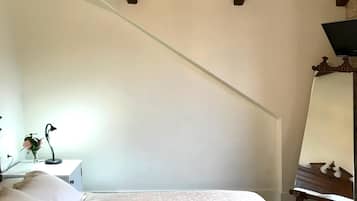 Un dormitorio con cama, una mesita de noche con lámpara, un espejo y una araña.