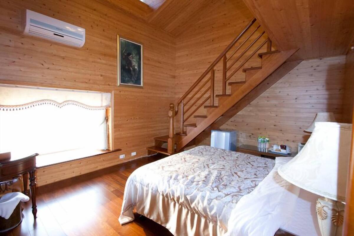 Una habitación de madera con cama, una silla, una mesa, una lámpara y una escalera.