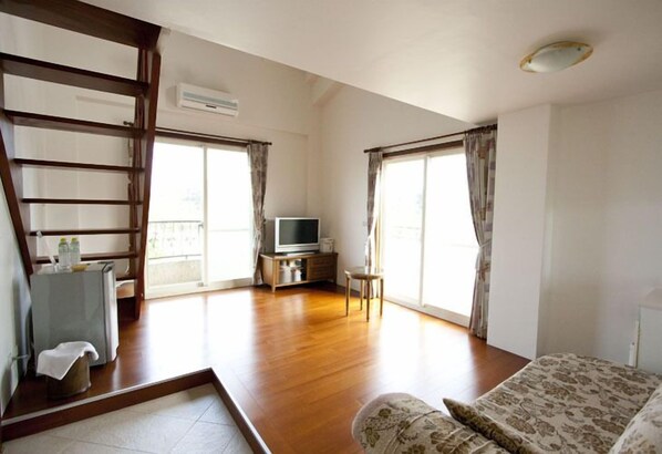 Um quarto espaçoso com piso de madeira, uma cama, uma televisão e uma varanda com cortinas.