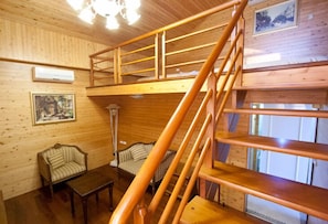 Ein Holzblock-Innenraum mit einer zentralen Treppe, zwei Sofas, einem Tisch und gerahmten Bildern an den Wänden.