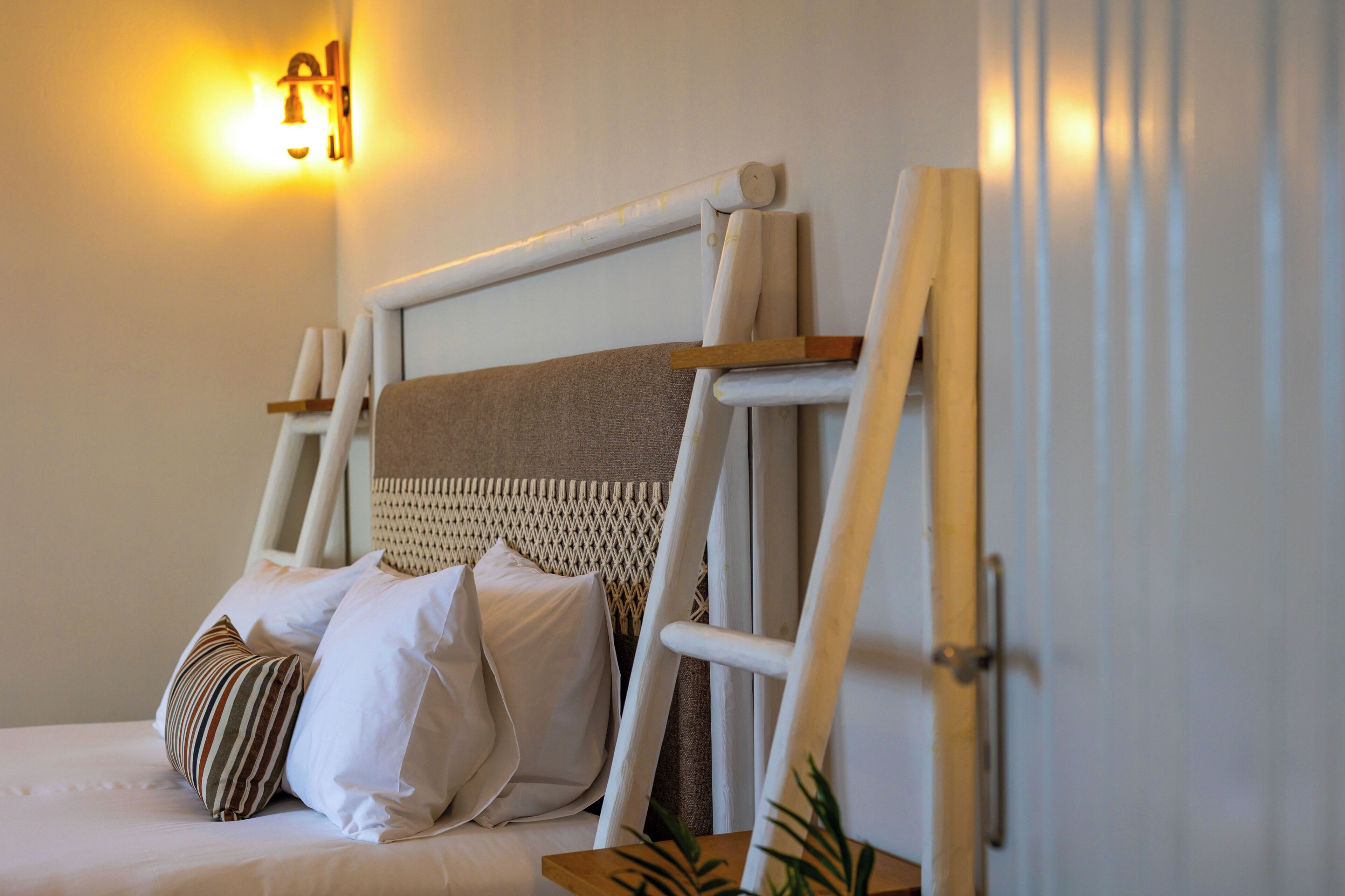 A neatly made bed with pillows, a headboard with a woven texture, and a wall-mounted light fixture.